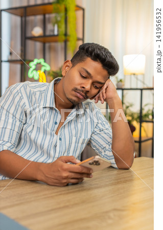 Indian man scrolls smartphone news feed bored frown unhappy tired mood burnout from endless updates Indian man scrolls smartphone news feed bored frown unhappy tired mood burnout from endless updates 141956532