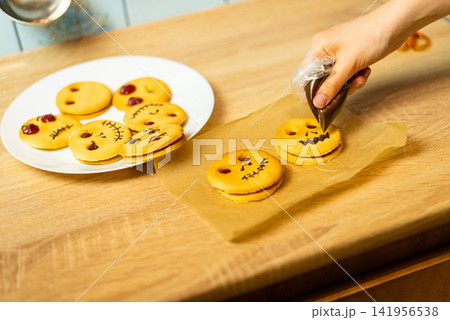 Hands decorating homemade Halloween cookies with chocolate glaze icing Hands decorating homemade Halloween cookies with chocolate glaze icing 141956538