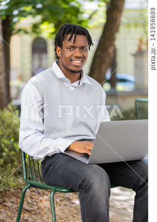 African American young man opening laptop for remote work in city street park outdoor urban travel African American young man opening laptop for remote work in city street park outdoor urban travel 141956689