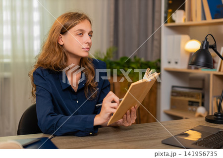 Young woman on home table reading study book marking key line while continuing calm learning process Young woman on home table reading study book marking key line while continuing calm learning process 141956735