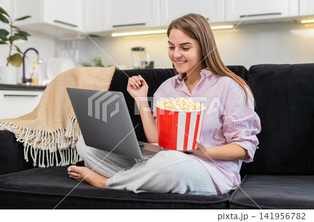 Young woman laughs out loud at laptop comedy with popcorn bucket and replays favorite funniest scene 141956782