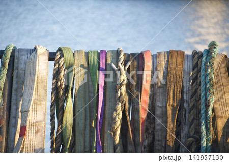 Weathered Ropes and Straps Hanging on Dock Railing by Calm Harbor Water at Sunset 141957130