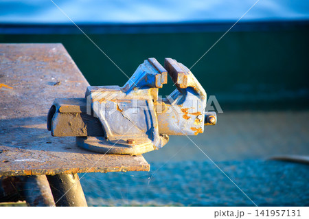 Rusty Blue Bench Vise On Weathered Workbench In Workshop With Sunlit Texture And Cobwebs Rusty Blue Bench Vise On Weathered Workbench In Workshop With Sunlit Texture And Cobwebs 141957131