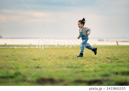 happy preschool child girl running on a grass field near river happy preschool child girl running on a grass field near river 141960205