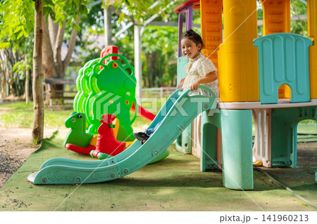 happy preschool child girl sliding down a playground slider. 141960213