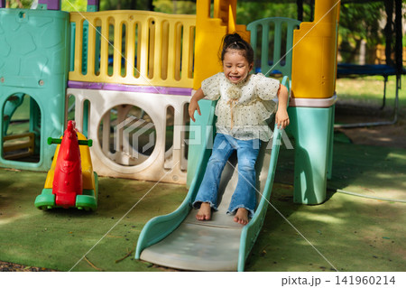 happy preschool child girl sliding down a playground slider. happy preschool child girl sliding down a playground slider. 141960214