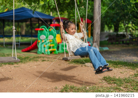 happy preschool child girl swinging on a wooden swing in a playground. happy preschool child girl swinging on a wooden swing in a playground. 141960215