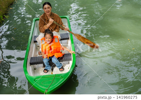 mother and preschool child girl in a green paddle boat on a scenic pond. mother and preschool child girl in a green paddle boat on a scenic pond. 141960275