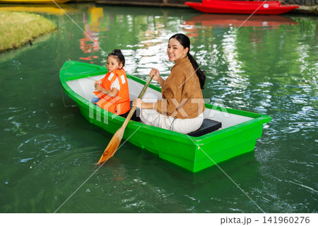 mother and preschool child girl in a green paddle boat on a scenic pond. 141960276