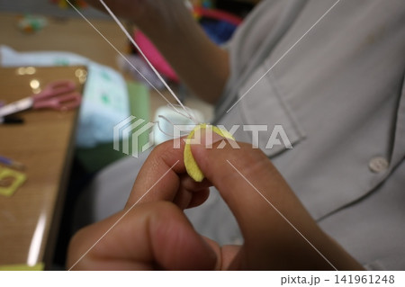 白衣を着た人が黄色フェルト指ぬきで手縫いをする様子 白衣を着た人が黄色フェルト指ぬきで手縫いをする様子 141961248