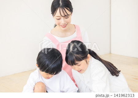 子供を優しく温かい笑顔で見守るピンクのエプロンを着た女性保育士 子供を優しく温かい笑顔で見守るピンクのエプロンを着た女性保育士 141962313