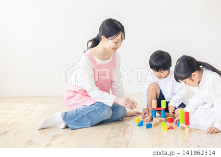 子供を優しく温かい笑顔で見守るピンクのエプロンを着た女性保育士 子供を優しく温かい笑顔で見守るピンクのエプロンを着た女性保育士 141962314