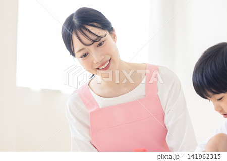子どもに優しく微笑みかけるピンクのエプロン姿の女性ヘルパー 141962315
