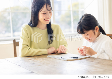リビングで母親に見守られながら指を使って一生懸命計算をする女の子 141962325