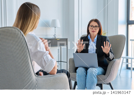 Professional female psychologist with laptop consulting young woman in modern clinic 141963147
