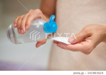 Woman's hands pouring micellar cleansing water from a bottle onto a cotton pad, performing a daily face care routine Woman's hands pouring micellar cleansing water from a bottle onto a cotton pad, performing a daily face care routine 141963824