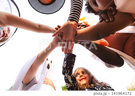Diverse children in Halloween costumes stacking hands for teamwork 141964172