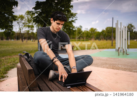 Young man using tablet as laptop on park bench Young man using tablet as laptop on park bench 141964180
