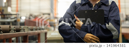 Mid-section body of female industrial worker in blue reflective uniform holding folder in factory. 141964381
