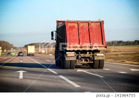 Rear view large red dump truck on asphalt highway. Heavy vehicle transporting cargo, road traffic, logistics, outdoor daytime. Rear view large red dump truck on asphalt highway. Heavy vehicle transporting cargo, road traffic, logistics, outdoor daytime. 141964755