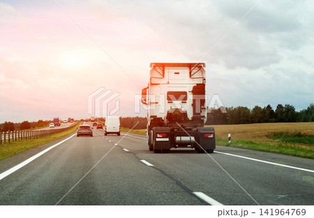White truck tractor unit driving on highway, back view of vehicle on road, many cars and trucks on a major route, transportation business, cargo shipping, industry logistics. Copy space for text 141964769