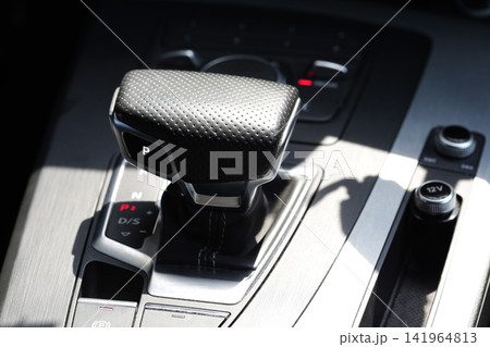 Modern car interior detail shot, automatic transmission gear shift lever displaying "P" for park, console controls, brushed metal finish, bright sunlight creating strong contrasts, automotive Modern car interior detail shot, automatic transmission gear shift lever displaying "P" for park, console controls, brushed metal finish, bright sunlight creating strong contrasts, automotive 141964813