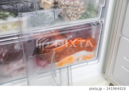 Close up view of broken plastic shelf inside refrigerator freezer compartment with frozen food packages, showing damage to appliance component and need for repair or replacement. 141964828