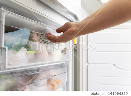 Human hand opening transparent drawer of modern white refrigerator freezer compartment filled with various frozen food items in plastic bags for storage and meal preparation Human hand opening transparent drawer of modern white refrigerator freezer compartment filled with various frozen food items in plastic bags for storage and meal preparation 141964829