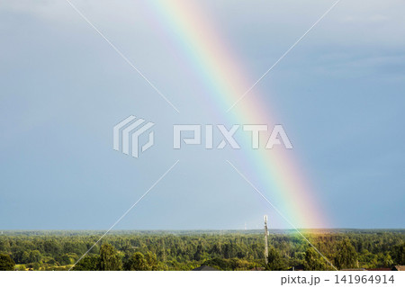 Bright colorful vibrant rainbow arc across expansive blue sky above lush green forest landscape featuring prominent modern mobile communication tower structure against horizon. Copy space Bright colorful vibrant rainbow arc across expansive blue sky above lush green forest landscape featuring prominent modern mobile communication tower structure against horizon. Copy space 141964914