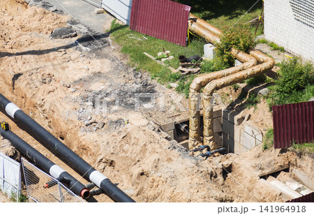Construction site featuring open trench excavation for pipeline installation, exposed heating mains and new utility pipes awaiting connection, illustrating urban infrastructure repair and maintenance 141964918
