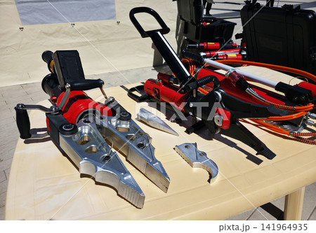 Hydraulic rescue tools equipment array display on table outdoor in daylight, featuring powerful spreaders and cutters used by emergency services for life saving operations and accident response 141964935