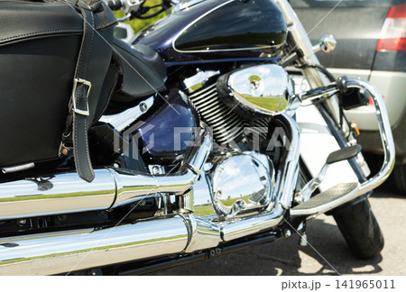 Side view of powerful cruiser motorcycle, highlighting shiny chrome exhaust pipes, intricate engine details, deep purple fuel tank with white stripe, and black leather saddlebag parked outdoors on Side view of powerful cruiser motorcycle, highlighting shiny chrome exhaust pipes, intricate engine details, deep purple fuel tank with white stripe, and black leather saddlebag parked outdoors on 141965011