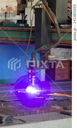 Plasma cutting machine in industrial workshop producing vibrant purple light during high-precision operation on metal sheet with intense sparks, showing modern manufacturing process vertical photo 141965059