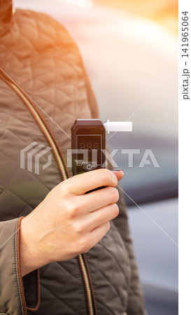 Close up view of person hand holding digital alcohol breathalyzer with empty display ready for test outdoors during day time, car background blurred, safety concept, vertical photo 141965064