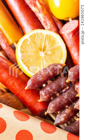 Assortment of gourmet dry cured sausages and meats with fresh lemon slice and yellow fruit, rustic food presentation, close up view vertical photo 141965073