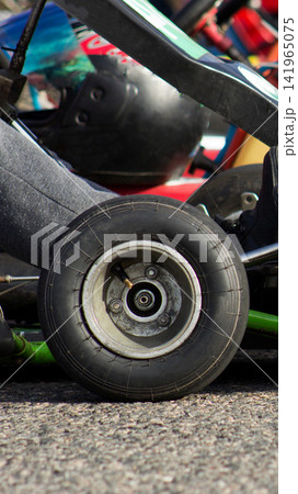 Close-up detail shot of go-kart front wheel with tire and part of chassis visible, showing driver leg wearing grey pants and racing helmet in background, ready for motorsport event vertical photo 141965075