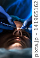 Doctor hands in blue gloves apply white strip on patient nose during medical examination procedure close up view dramatic lighting dark background, vertical photo, rhinoplasty, plastic surgery 141965162