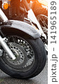 Motorcycle front wheel, fender, and disc brake detail with raindrops on glossy surface under warm sunlight flare, vertical shot of vehicle parts 141965189