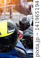 Neon yellow and black motorcycle helmet with raindrops on surface of blue motorbike parked outdoors. Sunlight shining on helmet and wet vehicle, reflecting light from wet surfaces. Ready for ride. 141965194