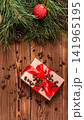 Christmas gift box with red ribbon and scattered pine nuts on rustic wooden table, adorned with pine branches, red ornament and pine cone, festive holiday background vertical photo 141965195