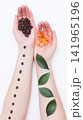 Caucasian hands hold roasted coffee beans and vibrant orange flower, parallel arms display raw coffee beans and fresh green leaves, symbolizing natural elements and daily routines, vertical photo 141965196