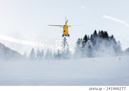 Scenic back view modern yellow rescue emergency mountain helicopter landing at forest ski slope at Alps mountain resort. Aviation transport machine silhouette alpine tourism service team Scenic back view modern yellow rescue emergency mountain helicopter landing at forest ski slope at Alps mountain resort. Aviation transport machine silhouette alpine tourism service team 141966277