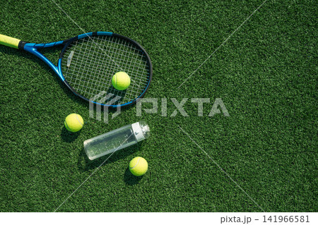 Tennis racket balls and water bottle on green grass court Tennis racket balls and water bottle on green grass court 141966581
