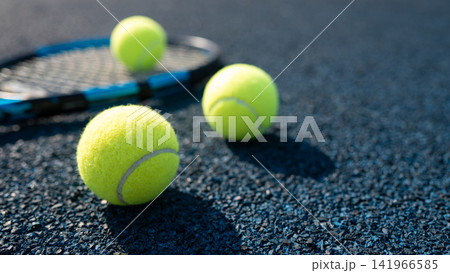 Tennis balls and racket on outdoor hard court in sunlight 141966585