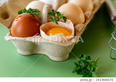 Fresh eggs in carton with whisk and herbs on green background Fresh eggs in carton with whisk and herbs on green background 141966678
