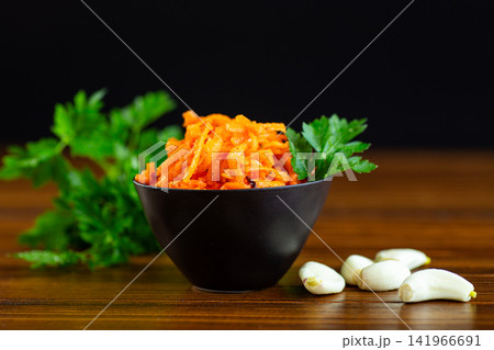 Fresh Korean carrot salad in dark bowl with green herbs Fresh Korean carrot salad in dark bowl with green herbs 141966691