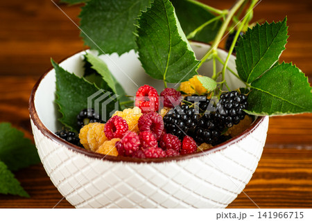 Organic mixed berries with green leaves in ceramic bowl on rustic wooden table Organic mixed berries with green leaves in ceramic bowl on rustic wooden table 141966715