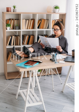 Corporate lifestyle. Employee routine. Pensive female manager analyzing business document using notebook laptop at desk at office. Corporate lifestyle. Employee routine. Pensive female manager analyzing business document using notebook laptop at desk at office. 141967452