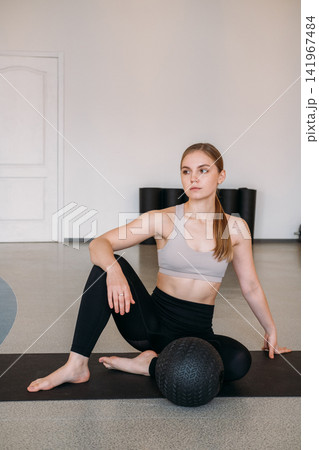 Female sport model. Pilates training. Confident bodybuilder sitting with professional gym gear in studio. Body strength physical therapy. 141967484