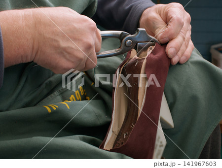 Fixing footwear. Professional shoemaker. Unrecognizable craftsman hands working with metal pliers at factory for handmade occupation. Fixing footwear. Professional shoemaker. Unrecognizable craftsman hands working with metal pliers at factory for handmade occupation. 141967603